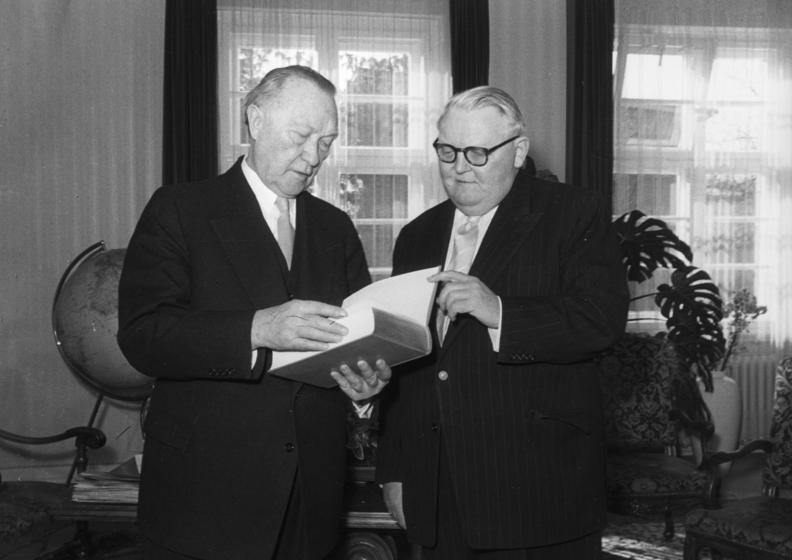 Bundeskanzler Konrad Adenauer liest interessiert in dem Buch, das ihm Bundes-Wirtschaftsminister Prof. Erhard als Geburtstagsgeschenk überreichte.