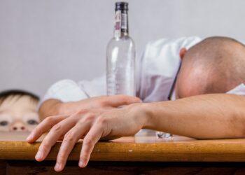 Kleines Kind schaut auf einen offenbar alkoholisierten Mann, der auf dem Tisch eingeschlafen ist