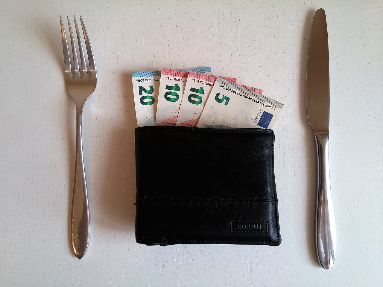 Mit Geldscheinen gefülltes Portemonnaie und seitlich davon liegen Messer und Gabel