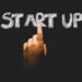 Finger zeigt auf eine Tafel mit dem Schriftzug "Start up"