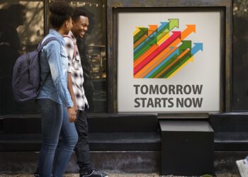 Junge Menschen vorm einem Werbeschild "Tomorrow starts now"