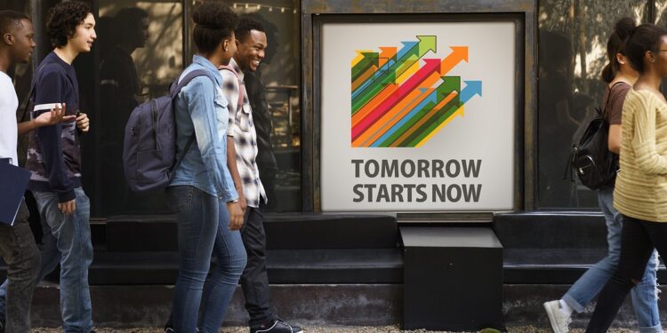 Junge Menschen vorm einem Werbeschild "Tomorrow starts now"