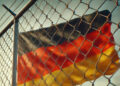 Deutschlandfahne hinter Maschen- und Stacheldrahtzaun, KI generiert