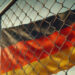 Deutschlandfahne hinter Maschen- und Stacheldrahtzaun, KI generiert
