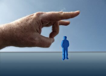 Große Hand, die dabei ist, eine kleine blaue Spielfigur wegzuschnippen. Symbolbild für die Pläne der AfD, mit Arbeitslosen umzugehen