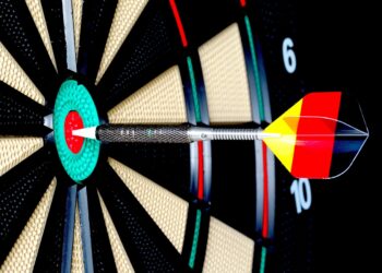 Dartpfeil mit Federn in den Deutschlandfarben trifft in die Mitte einer Dartscheibe