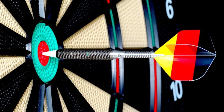 Dartpfeil mit Federn in den Deutschlandfarben trifft in die Mitte einer Dartscheibe