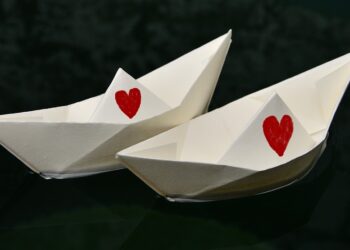 Zwei weiße Papierschiffchn mit jeweils einem großen, roten Herz in der Mitte