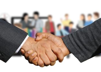 Händedruck zwischen zwei Männerhänden, im Hintergrund eine Personengruppe