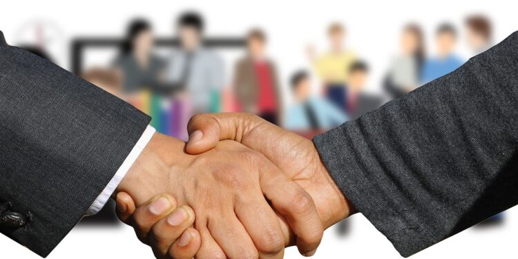 Händedruck zwischen zwei Männerhänden, im Hintergrund eine Personengruppe