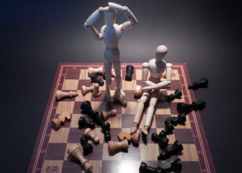 Schachspiel mit lauter ugeworfenen Speilfiguren und 2 Holzpupen, die auf dem Schachbrett stehen bzw. sitzen.