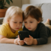 Zwei kleine Kinder liegen auf dem Sofa und starren auf ein Smartphone-Bildschirm, KI generiert