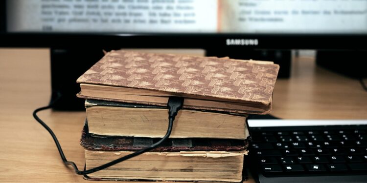 alte Bücher vorneinem Computerbildschirm und mit einem Netzkabel verbunden
