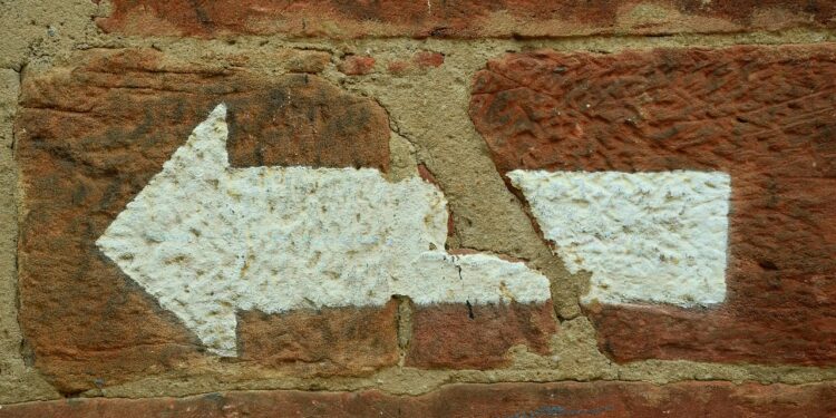 Weißer Abbiegepfeil nach links auf roter Ziegelsteinmauer
