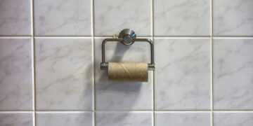 Leere Klopapierrolle an Halter vor gefliester Wand