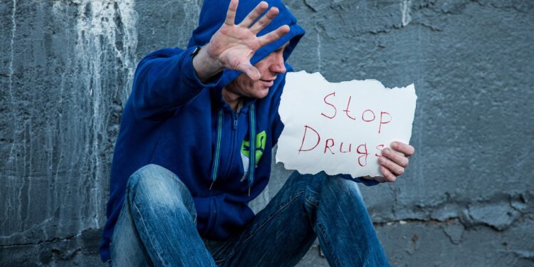 Symbolbild: Süchtiger Mann hebt abwehrend die Hand und hält in der anderen Hand ein Bild "Stop Drugs"