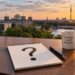 Skyline von Berlin, davor ein Schreibtisch mit einem Schreibblock, auf dem ein großes Fragezeichen steht. KI generiert mit ChatGPT.